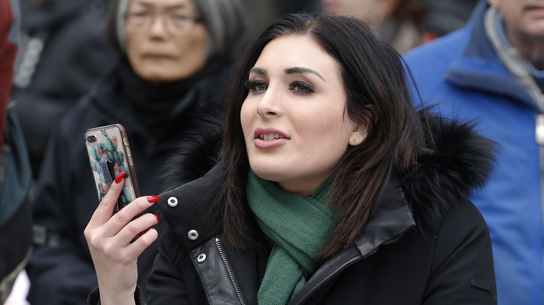 Laura Loomer outside holding up her cell phone in a crowd