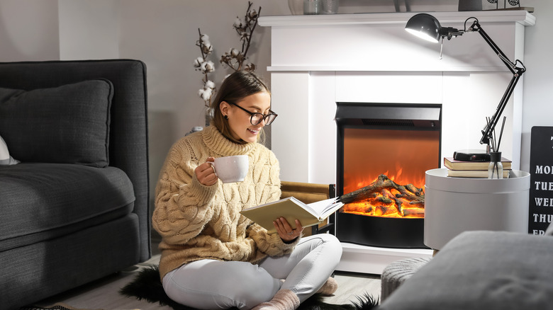 Woman reading a book in front of the fireplace 