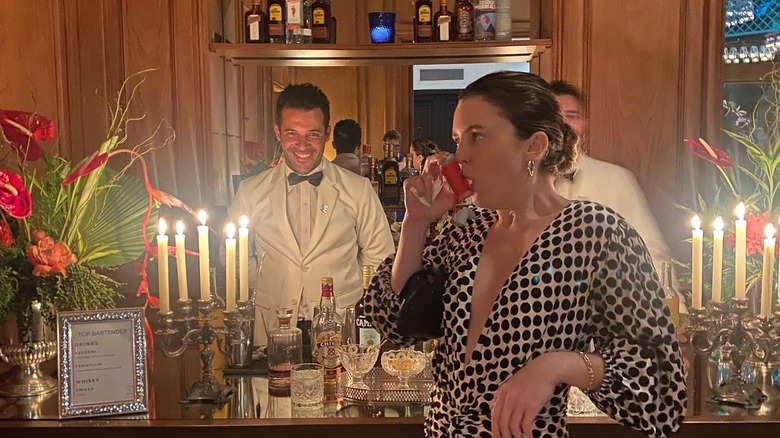 Lorraine Nicholson takes her inhaler at a fancy bar with bartenders in tuxedos in the background