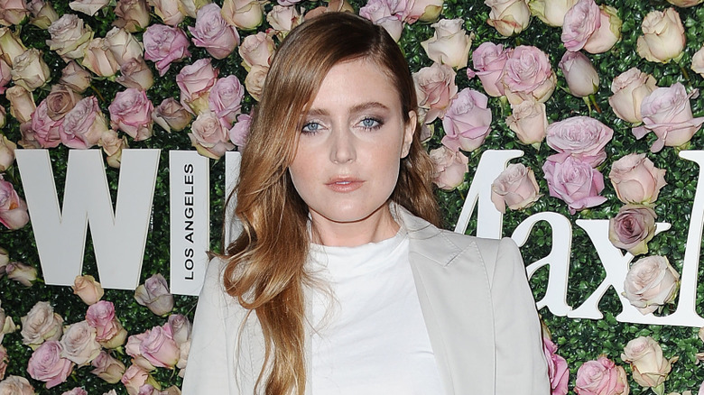 Lorraine Nicholson stands in front of a wall of flowers posing at an event