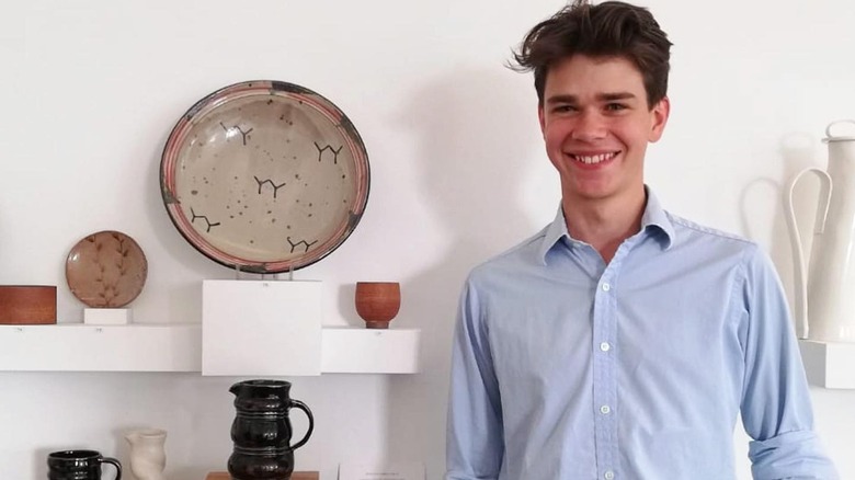 Sam Chatto smiles in front of his pottery pieces on display.