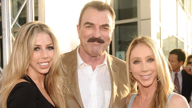 Hannah Selleck smiles on the red carpet next to her parents in the sun.