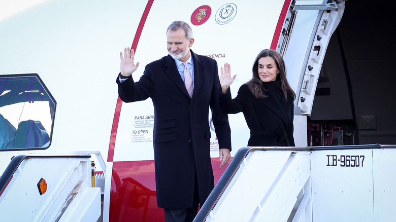 King Felipe and Queen Letizia waving behind them as they board a plane