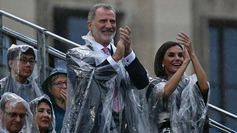 King Felipe and Queen Letizia clapping in plastic ponchos in the rain at the opening ceremony of 2024 Paris Olympics