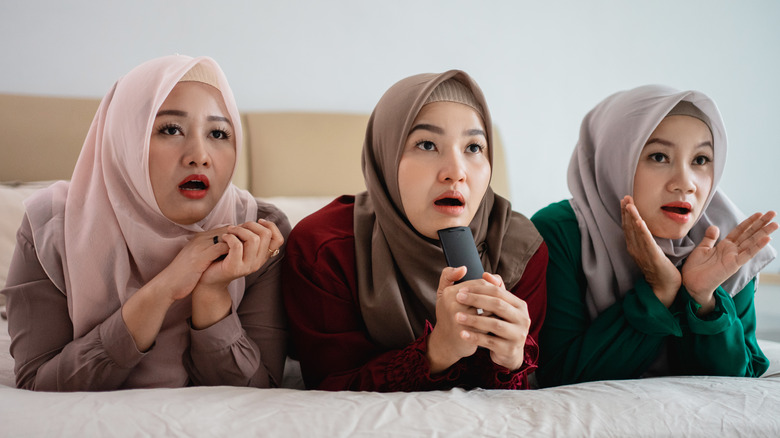 Three women in hijabs looking engrossed at off-screen TV