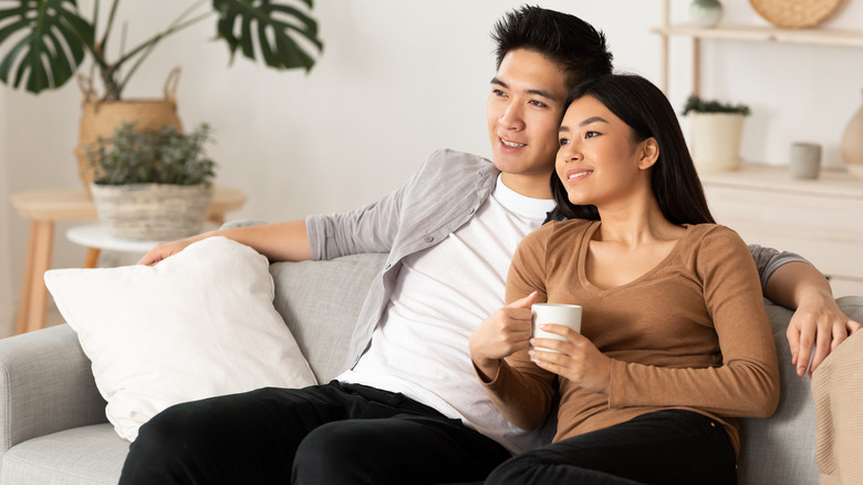 Smiling heterosexual Asian couple sitting on couch together