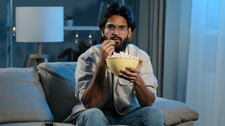 man eating popcorn on couch