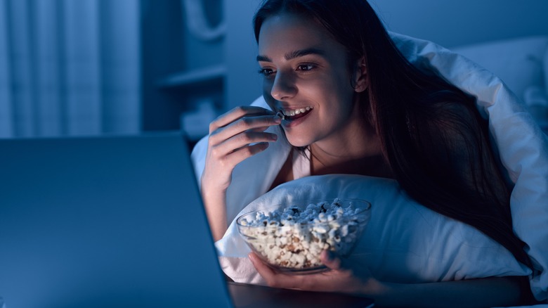 Woman watching laptop, eating popcorn