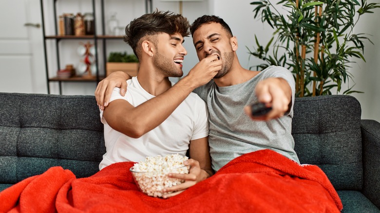 Hispanic homosexual couple eating popcorn and watching movie together