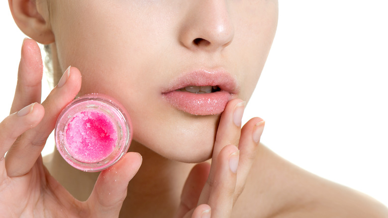 Close up of woman holding up a pink exfoliating lip sugar scrub, applying to her lips