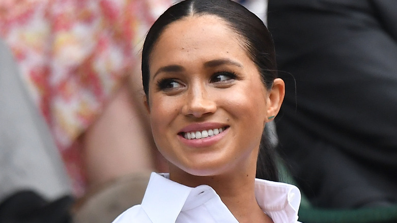 Meghan Markle poses with her hair pulled back and a smile.