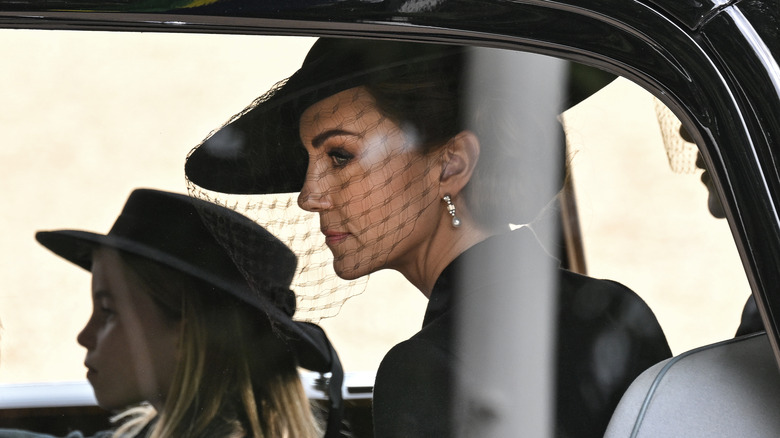 Kate Midleton looking serious in black veil riding in car