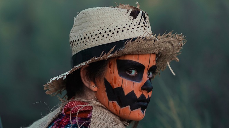 Person looking over shoulder with straw hat and pumpkin makeup