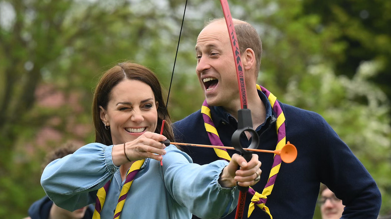 Kate Middleton doing archery while Prince William laughs