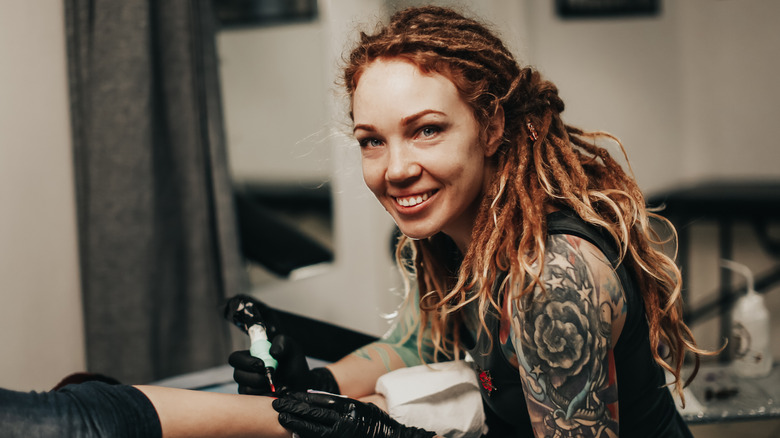 woman smiling while tattooing client's arm