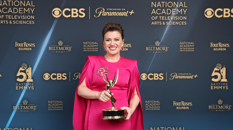 Kelly Clarkson holding an Emmy on the red carpet in pink dress