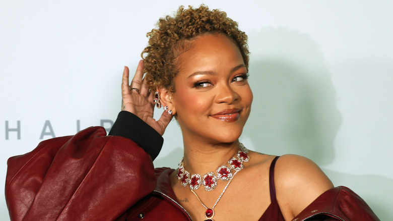 Rihanna smiling on step-and-repeat with hand to head showing off her short curly hair