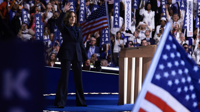 Kamala Harris waving on stage surrounded by crowds and American flags