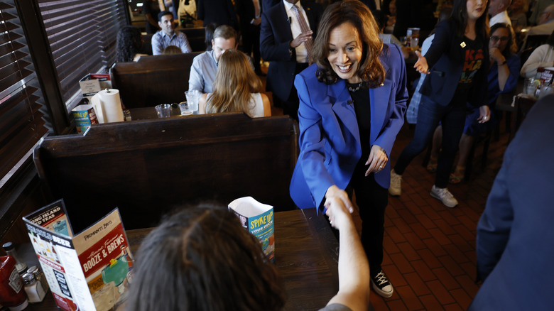 Kamala Harris shaking hands with woman sitting in crowded restaurant