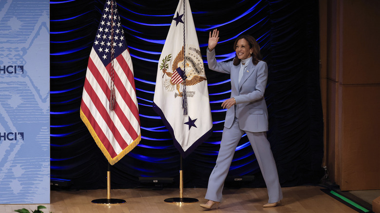 Kamala Harris waving as she walks past American flag