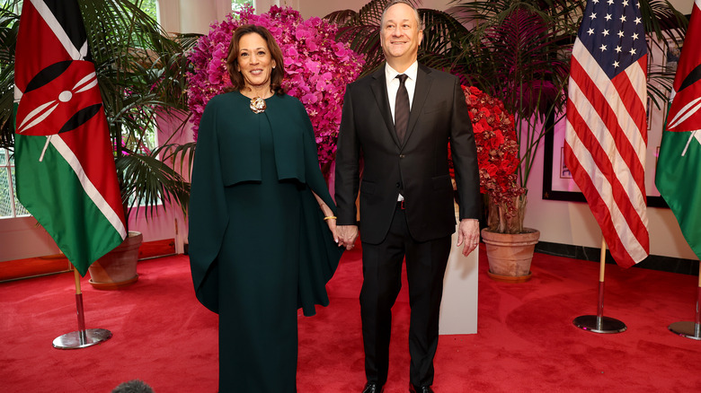 Kamala Harris and Doug Emhoff holding hands posing between U.S. and Kenya flags