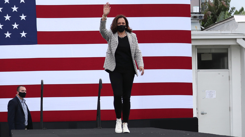 Kamala Harris waving stage in front of an American flag