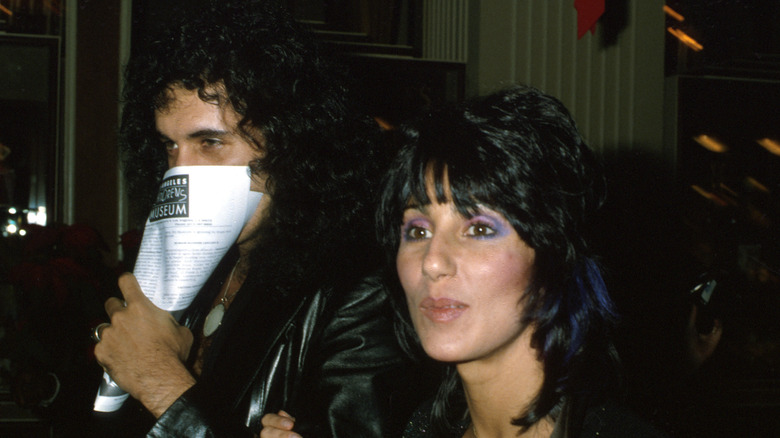 Gene Simmons covering his face walking next to Cher