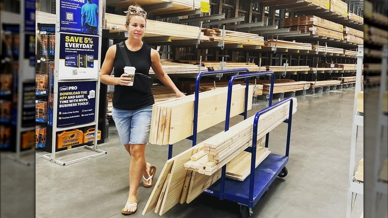 Jana Duggar wearing tank top and shorts pushing lumber trolley