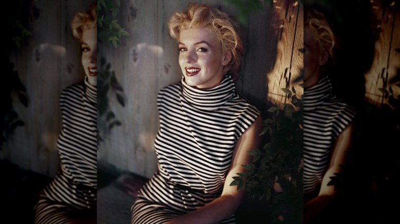 Marilyn Monroe wearing a striped dress, sitting down, smiles for the camera