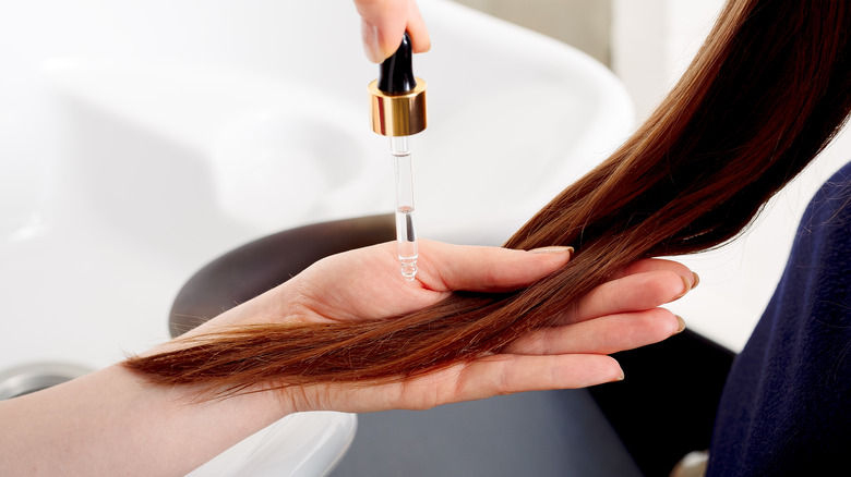 hands applying oil on long brown hair