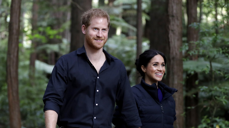 Prince Harry and Meghan Markle smiling while walking in the woods