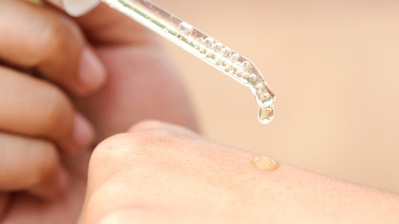 Woman putting vitamin C serum on back of hand