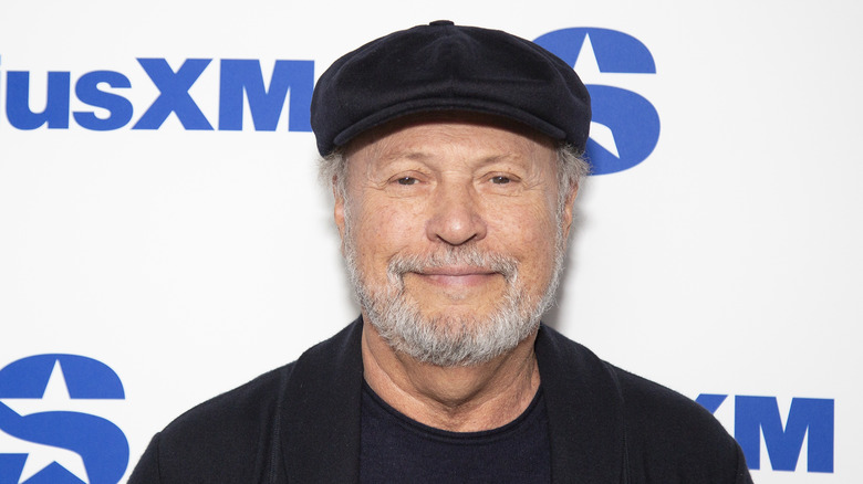 Billy Crystal smiling in a black cap