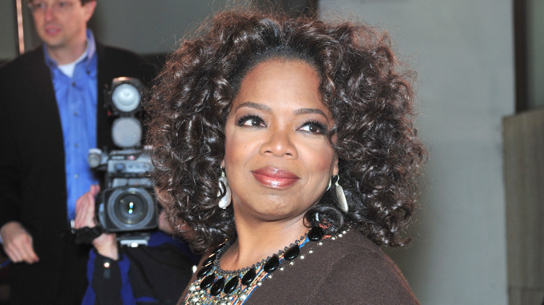 Oprah smiles while looking over her shoulder wearing a statement necklace.