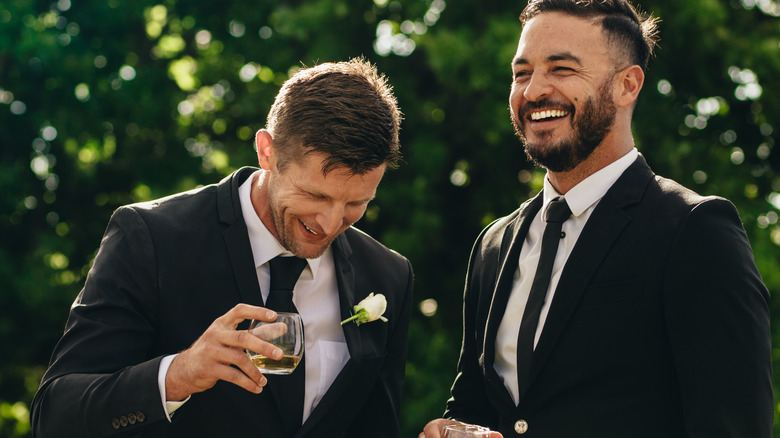 Groom and best man laugh, holding drinks