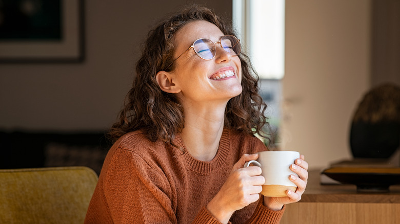 A person happily drinking a cup of coffee with a big smile of their face