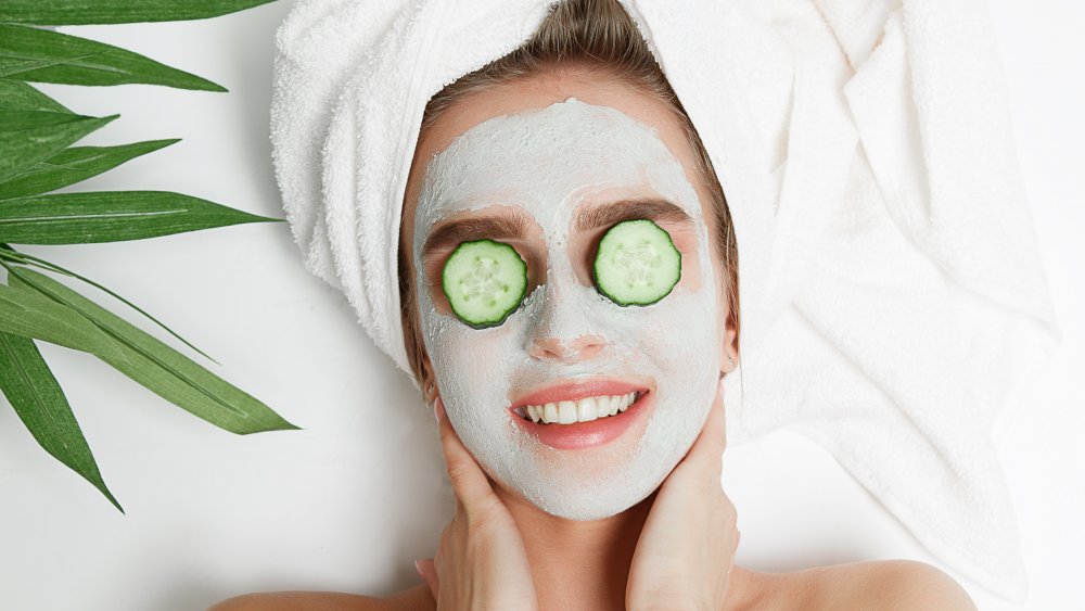 A woman wearing a face mask with cucumbers over her eyes