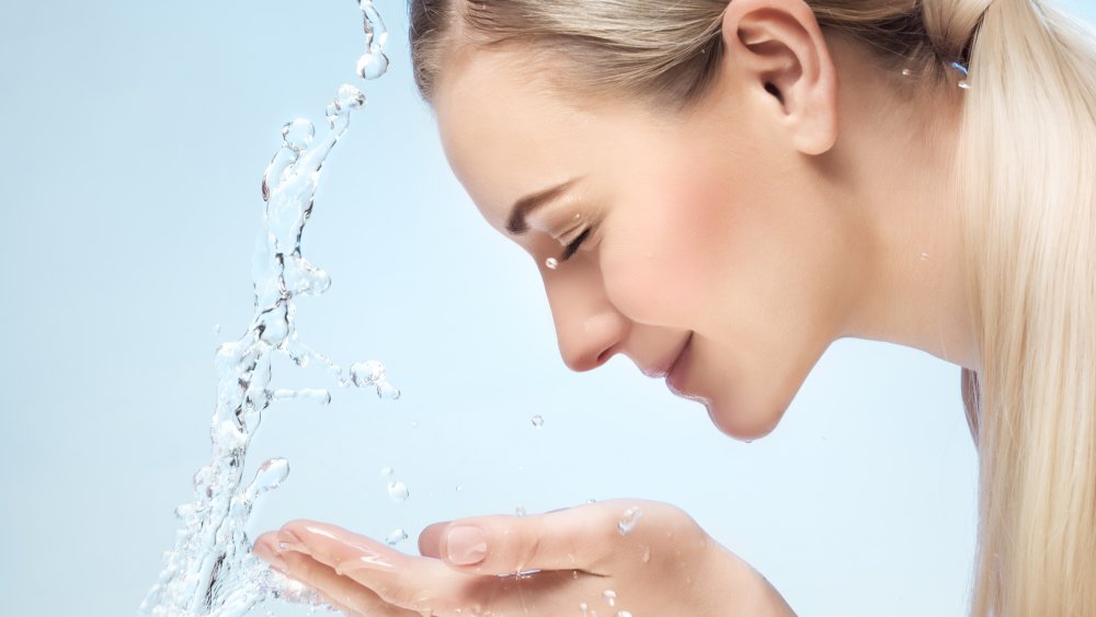 A woman washing her face, eyes closed