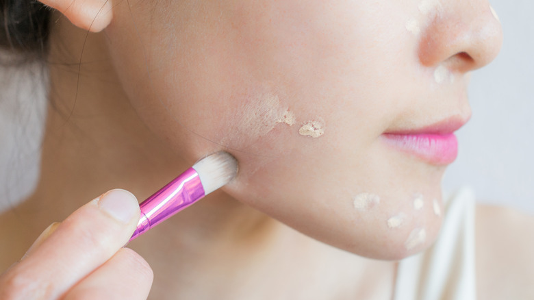 A woman blending concealer with small brush 