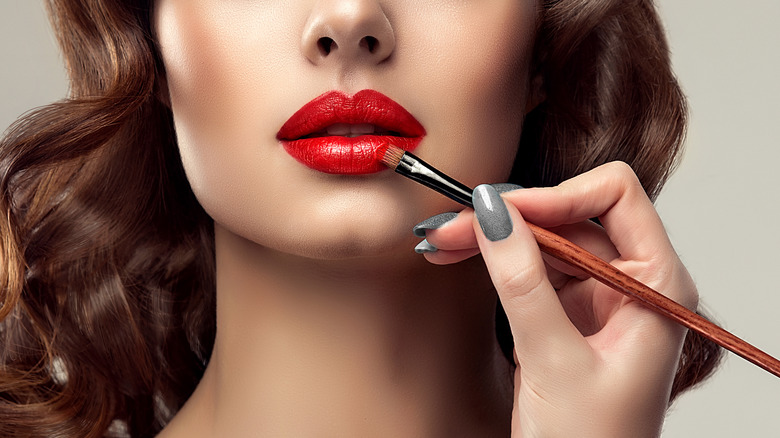 Red lipstick being applied with makeup brush 