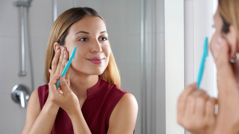 Woman dermaplaning in mirror 