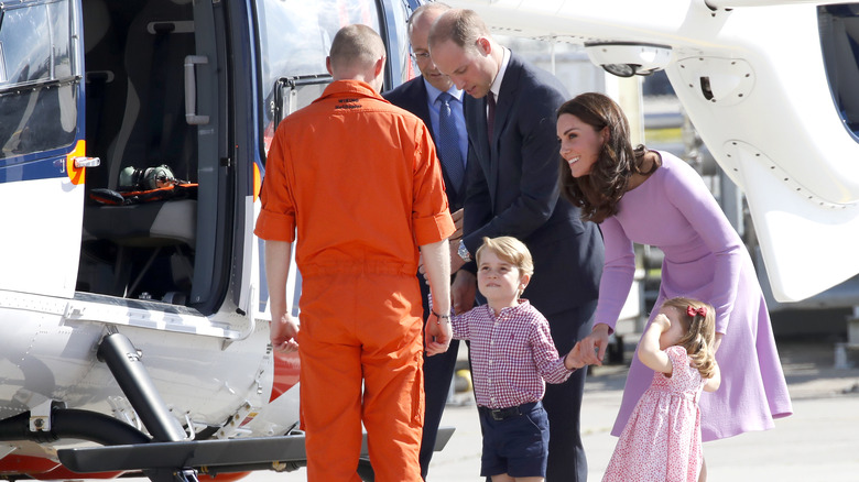 Prince William and Kate Middleton standing near a helicopter with their children. 