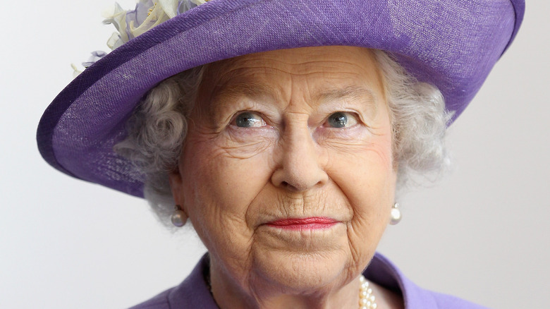 Queen Elizabeth wearing a purple hate and pink lipstick