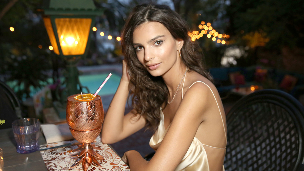 Model Emily Ratajkowski sitting at a table with a tall drink