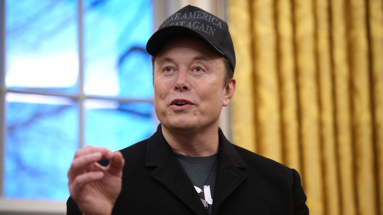 Elon Musk talking in a black MAGA hat