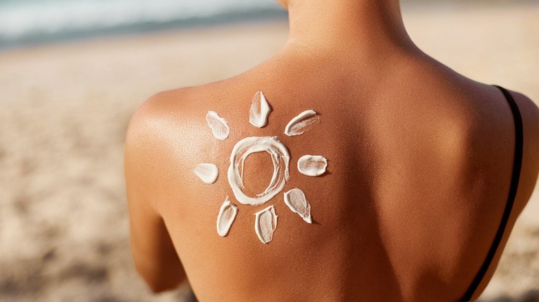 Women sitting on beach with sunscreen on her back. 