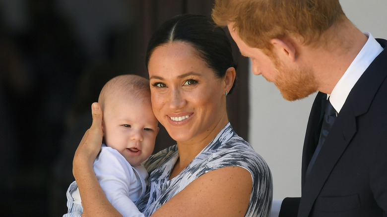 Prince Harry stares at his wife, Meghan Markle who smiles holding their baby, Archie