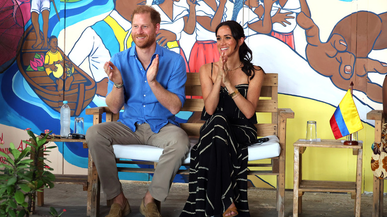 Prince Harry smiles sitting next to his wife, Meghan Markle