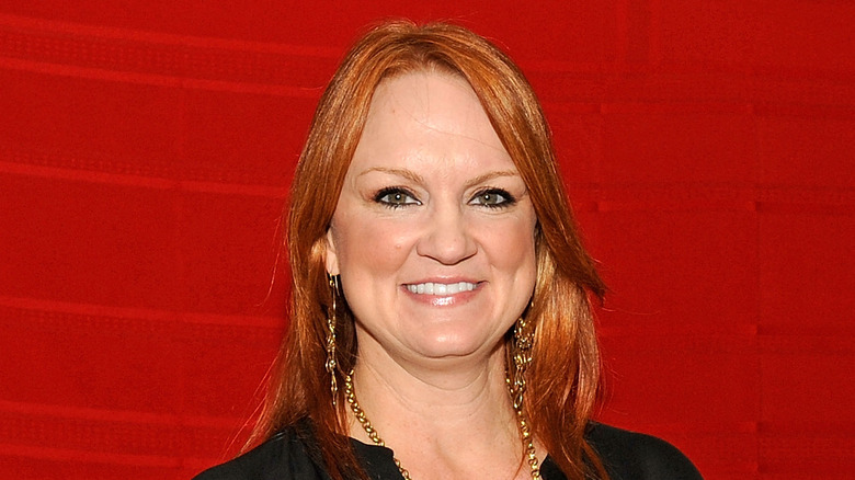 Ree Drummond poses against a red background wearing black and a big smile.