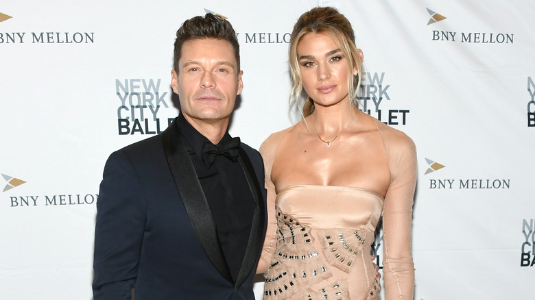 Ryan Seacrest stares forward with Shayna Taylor in a nude dress with crystals.